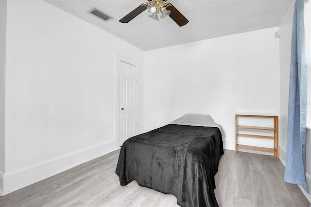 bedroom featuring ceiling fan, light hardwood / wood-style floors, and a textured ceiling