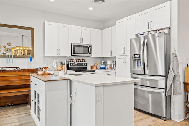 kitchen featuring light hardwood / wood-style floors, white cabinets, a kitchen island with sink, and appliances with stainless steel finishes