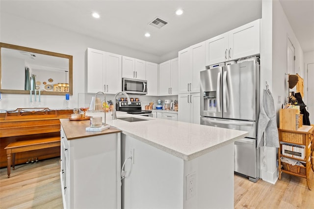 kitchen with white cabinetry, appliances with stainless steel finishes, kitchen peninsula, sink, and light hardwood / wood-style flooring