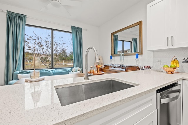 kitchen with light stone counters, stainless steel dishwasher, white cabinetry, ceiling fan, and sink