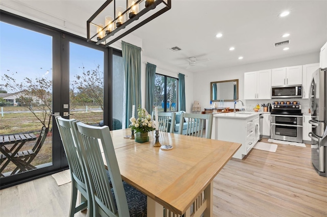 dining area with ceiling fan with notable chandelier, light wood-type flooring, and sink