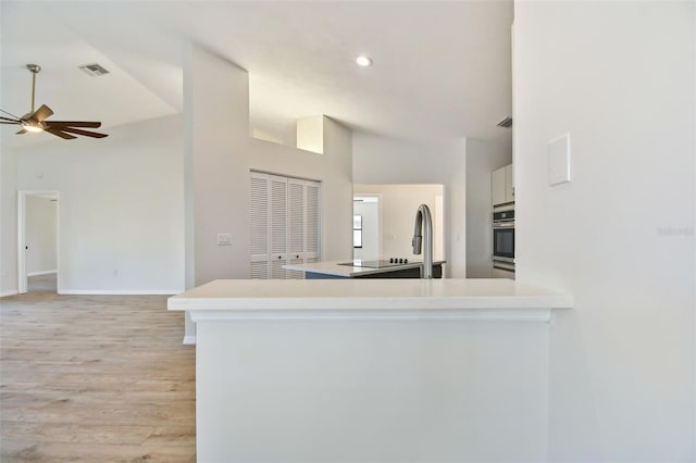 kitchen with high vaulted ceiling, white cabinets, oven, ceiling fan, and kitchen peninsula