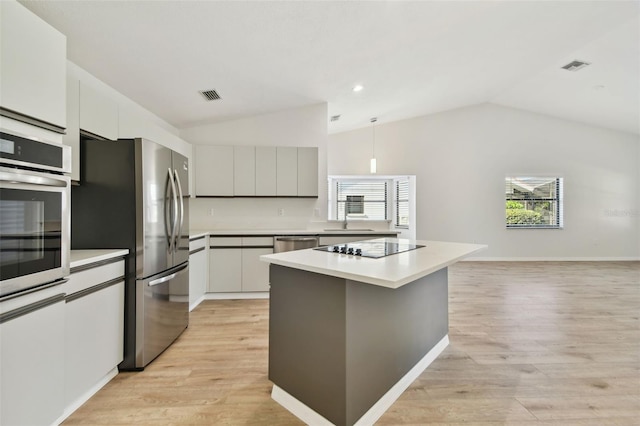 kitchen with lofted ceiling, appliances with stainless steel finishes, a kitchen island, and light hardwood / wood-style flooring