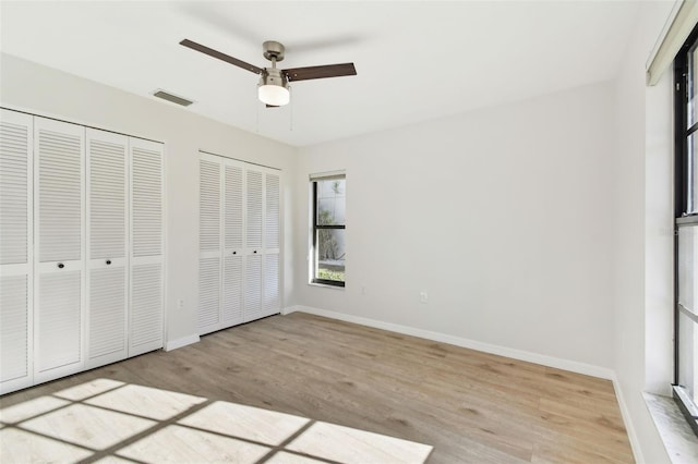 unfurnished bedroom with two closets, light hardwood / wood-style floors, and ceiling fan