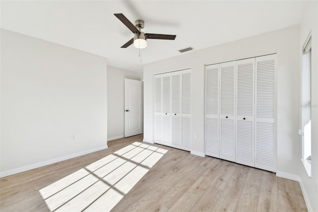 unfurnished bedroom with two closets, light hardwood / wood-style flooring, and ceiling fan