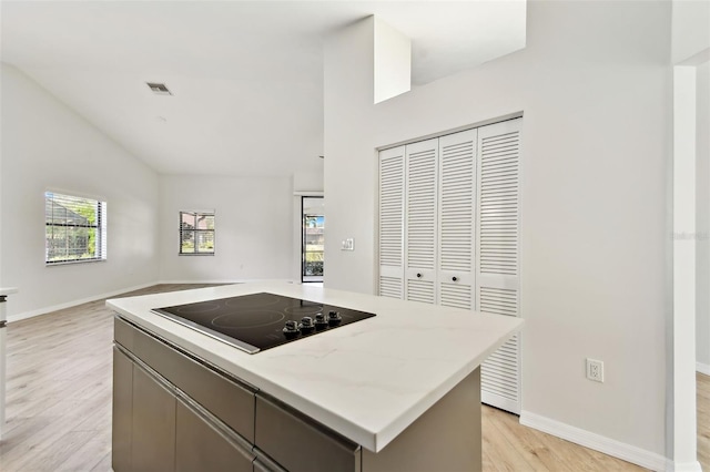 kitchen with lofted ceiling, black electric stovetop, a kitchen island, and light hardwood / wood-style flooring