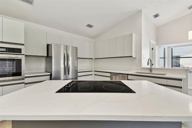 kitchen with sink, hanging light fixtures, stainless steel appliances, light stone countertops, and vaulted ceiling