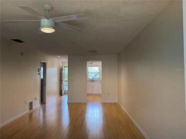 empty room with a textured ceiling, ceiling fan, and light hardwood / wood-style flooring