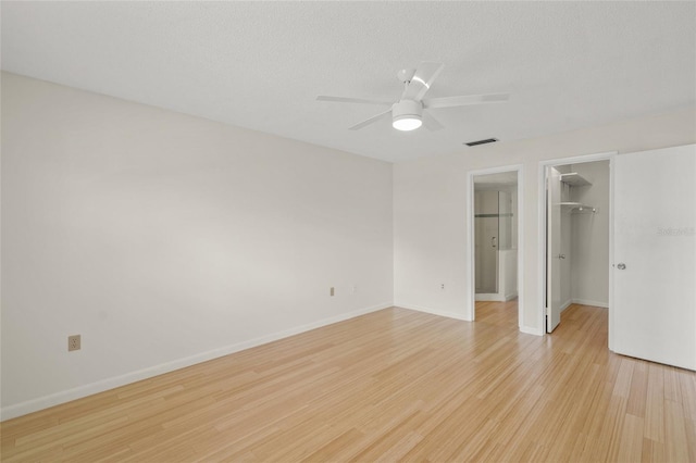 unfurnished bedroom with ceiling fan, light hardwood / wood-style floors, a textured ceiling, a spacious closet, and a closet