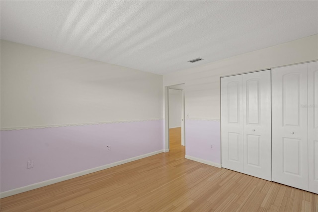 unfurnished bedroom featuring a closet, a textured ceiling, and light wood-type flooring