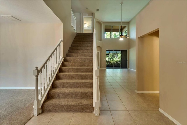 staircase with tile patterned flooring, ceiling fan, and a high ceiling