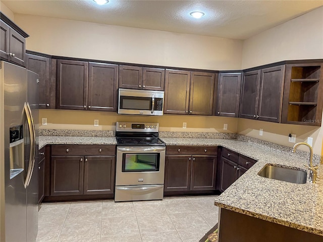 kitchen with dark brown cabinetry, light stone countertops, sink, stainless steel appliances, and light tile patterned floors