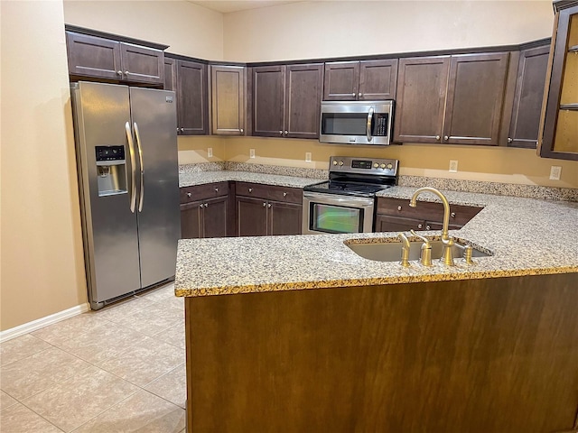 kitchen with dark brown cabinetry, light stone countertops, sink, stainless steel appliances, and kitchen peninsula