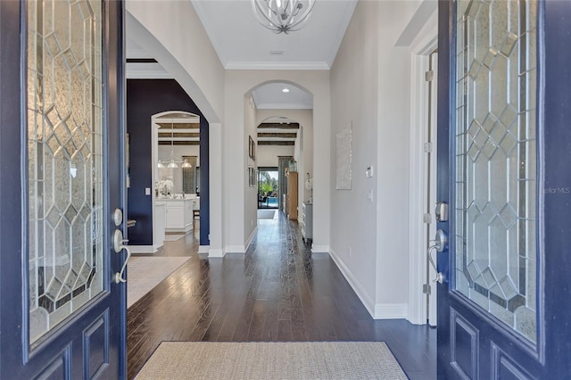 foyer entrance with an inviting chandelier, beam ceiling, ornamental molding, and dark hardwood / wood-style floors