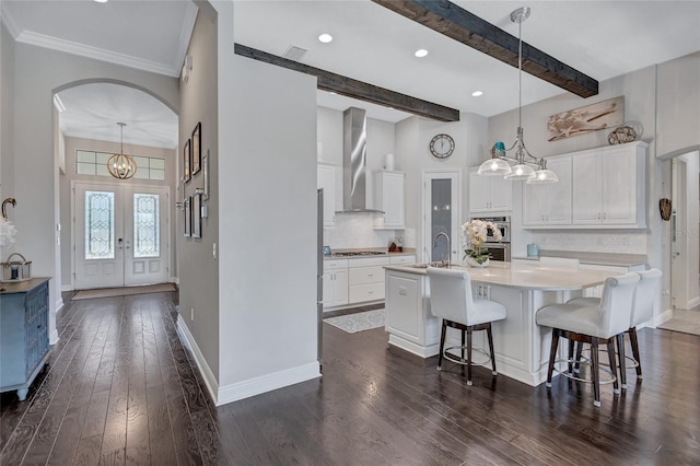 kitchen featuring white cabinets, an island with sink, french doors, and wall chimney exhaust hood