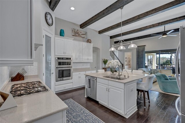 kitchen with a center island with sink, stainless steel appliances, hanging light fixtures, white cabinets, and sink