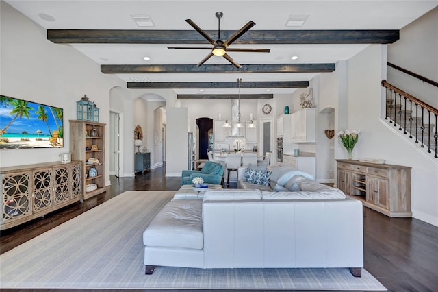 living room with ceiling fan with notable chandelier, beam ceiling, and dark hardwood / wood-style flooring