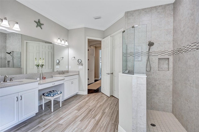 bathroom with hardwood / wood-style floors, a tile shower, crown molding, and vanity