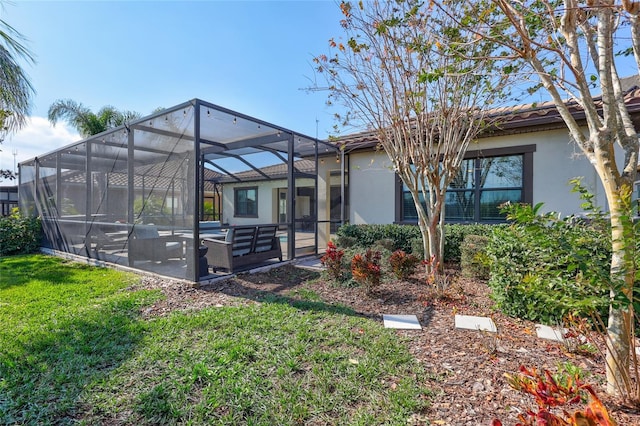 back of property featuring a lawn, glass enclosure, and a patio