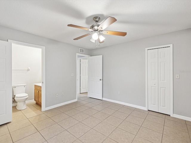 unfurnished bedroom with ceiling fan, light tile patterned floors, a closet, and ensuite bathroom