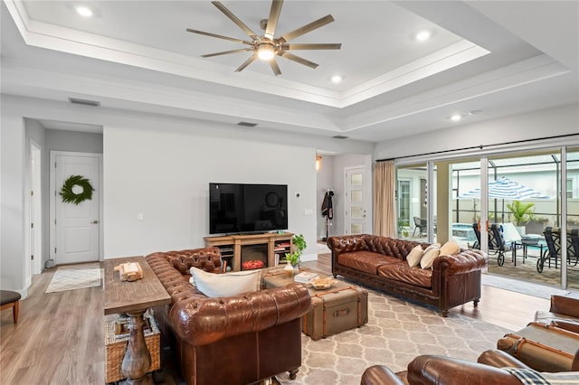 living room featuring crown molding, ceiling fan, a tray ceiling, and light hardwood / wood-style flooring