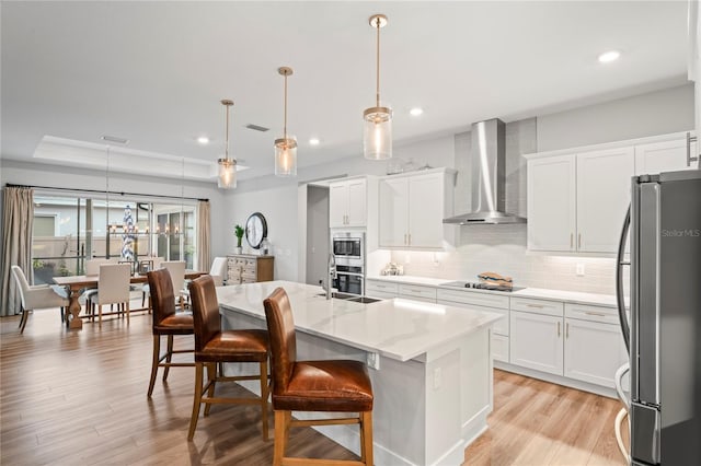 kitchen featuring stainless steel appliances, hanging light fixtures, white cabinets, and wall chimney exhaust hood