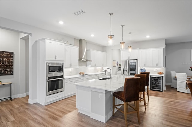 kitchen featuring a large island, wall chimney range hood, stainless steel appliances, and white cabinets