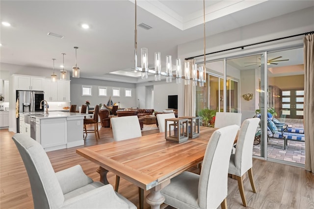 dining area featuring a raised ceiling, ceiling fan, and light wood-type flooring