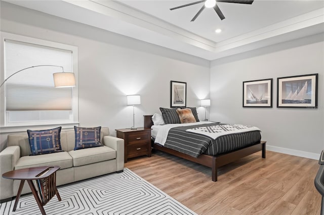 bedroom featuring ceiling fan, a raised ceiling, and light hardwood / wood-style floors