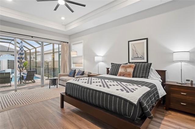 bedroom featuring light hardwood / wood-style flooring, a tray ceiling, access to outside, and ceiling fan