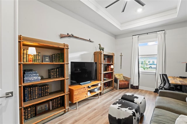 living room featuring a raised ceiling, ceiling fan, and light wood-type flooring