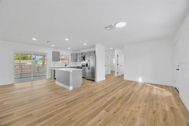 kitchen with appliances with stainless steel finishes, a kitchen island, sink, gray cabinets, and light hardwood / wood-style flooring