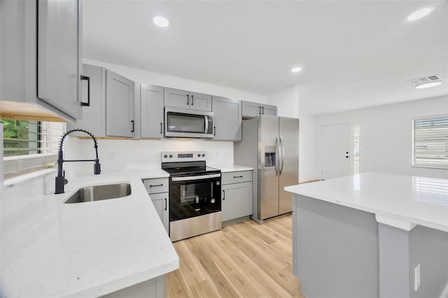 kitchen with light wood-type flooring, appliances with stainless steel finishes, sink, and gray cabinetry