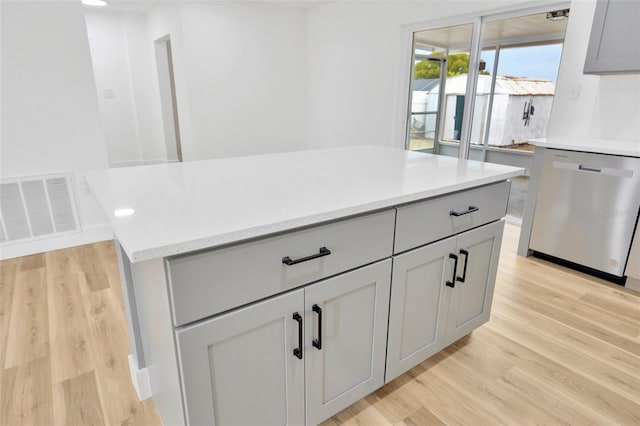 kitchen featuring gray cabinetry, light wood-type flooring, a kitchen island, stainless steel dishwasher, and light stone counters