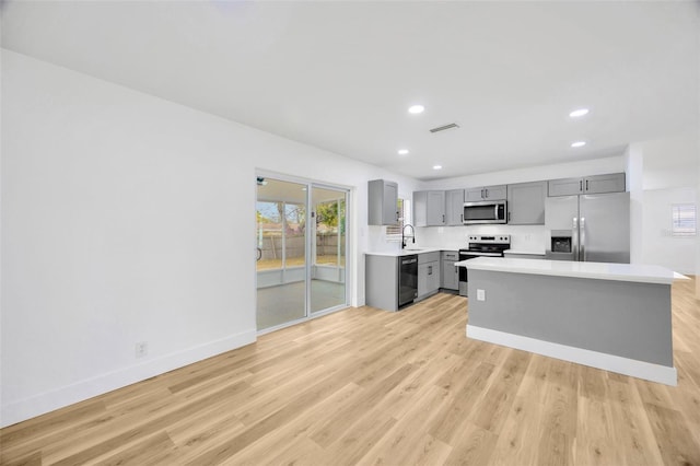 kitchen with tasteful backsplash, sink, light hardwood / wood-style flooring, gray cabinetry, and stainless steel appliances