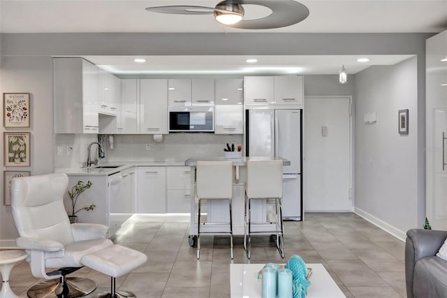 kitchen featuring white cabinetry, ceiling fan, white appliances, a breakfast bar, and sink