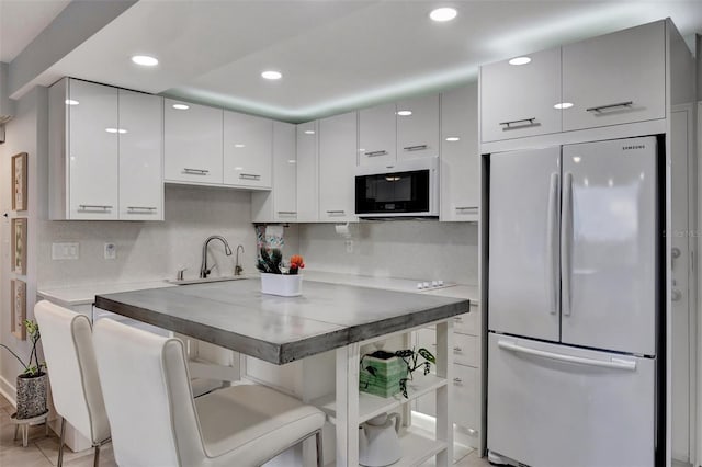 kitchen featuring white appliances, white cabinets, decorative backsplash, sink, and a breakfast bar