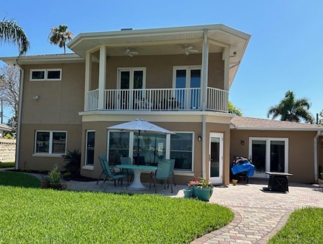 rear view of property with a balcony, a patio, ceiling fan, and a lawn