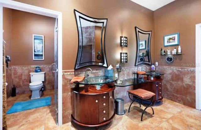 bathroom with toilet, vanity, and tile walls