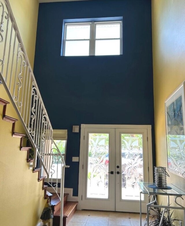 entryway featuring a high ceiling, light tile patterned flooring, french doors, and a healthy amount of sunlight