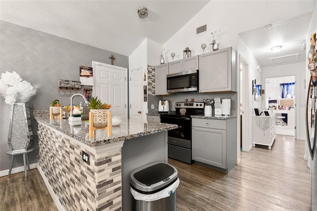 kitchen with lofted ceiling, gray cabinetry, light stone counters, dark hardwood / wood-style flooring, and stainless steel appliances