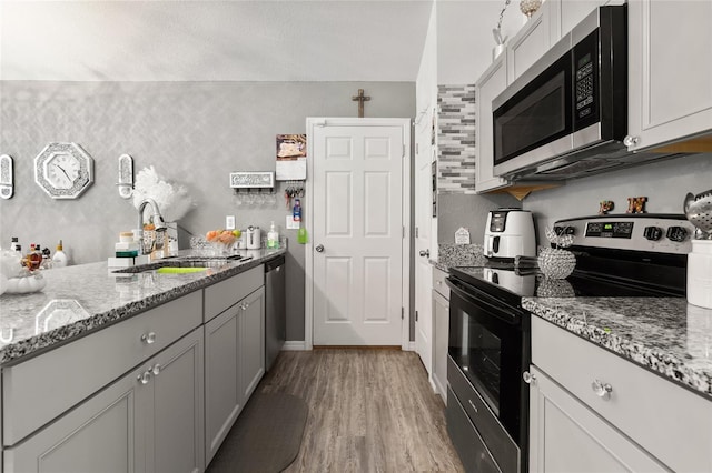 kitchen with appliances with stainless steel finishes, light stone countertops, sink, and light wood-type flooring