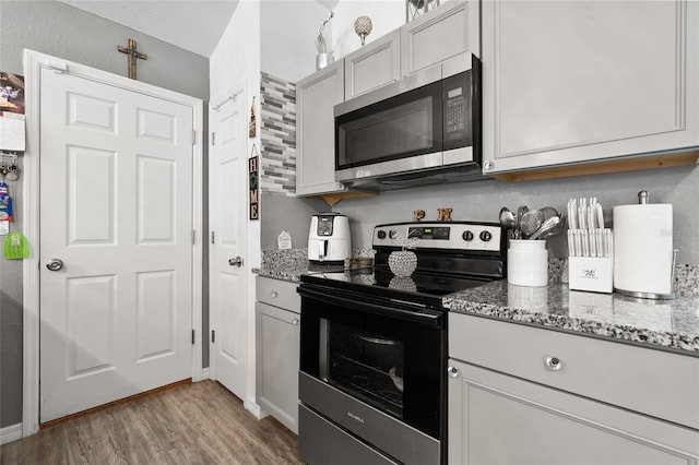 kitchen with stainless steel appliances, dark stone counters, and light wood-type flooring