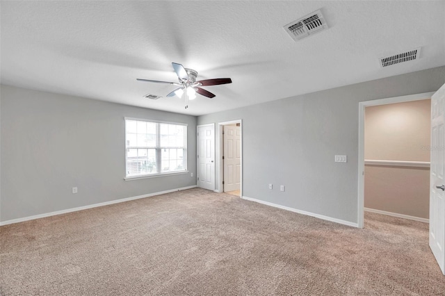 unfurnished bedroom with a walk in closet, light colored carpet, a textured ceiling, a closet, and ceiling fan