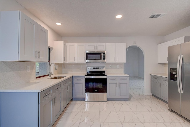 kitchen featuring gray cabinets, tasteful backsplash, sink, stainless steel appliances, and a textured ceiling