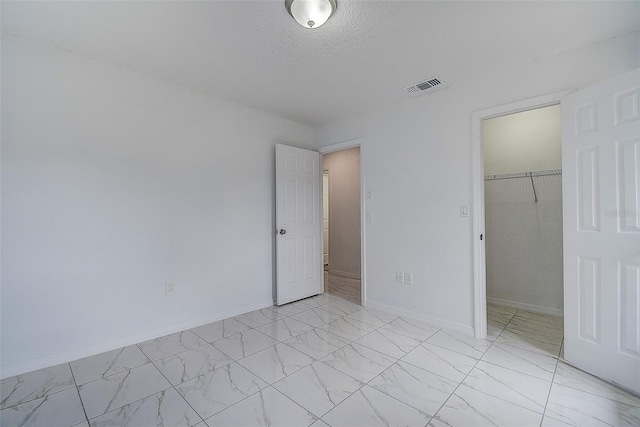 unfurnished bedroom featuring a spacious closet, a closet, and a textured ceiling