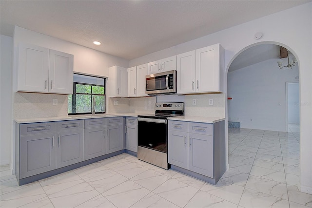 kitchen with stainless steel appliances, gray cabinets, white cabinets, and backsplash