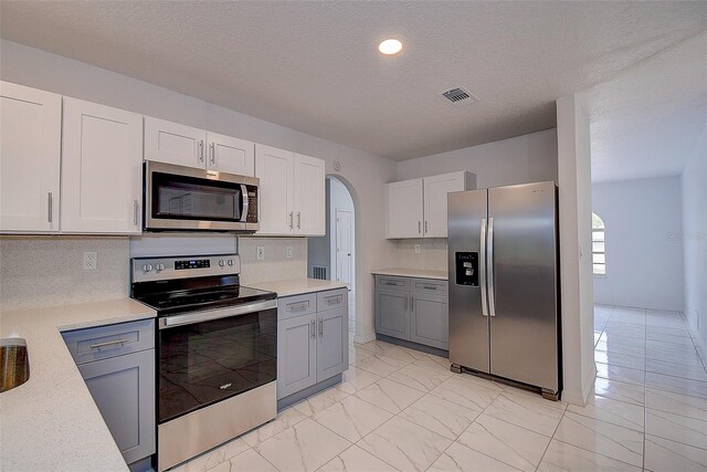 kitchen with white cabinetry, tasteful backsplash, gray cabinetry, and appliances with stainless steel finishes