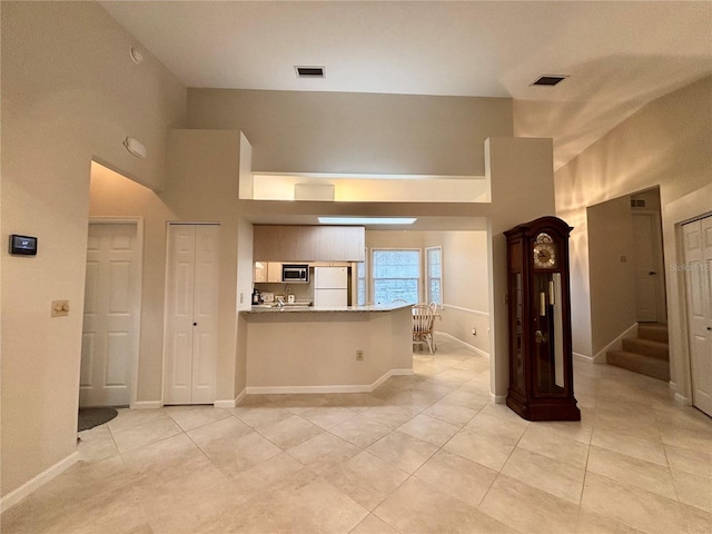 kitchen with kitchen peninsula, stainless steel microwave, light tile patterned flooring, a towering ceiling, and white refrigerator