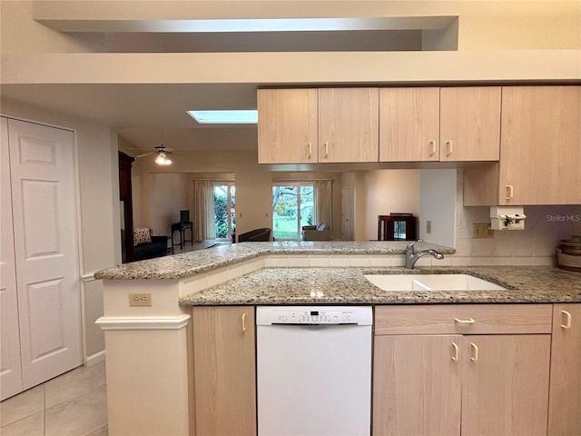 kitchen featuring a skylight, kitchen peninsula, light brown cabinetry, dishwasher, and sink